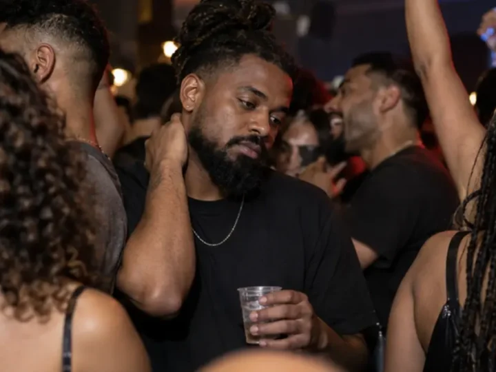 Homem segura um copo e observa outras pessoas conversando num encontro movimentado