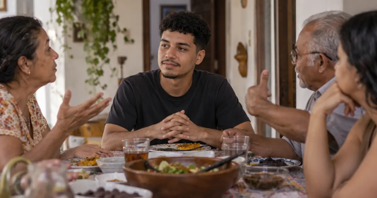Jovem de camiseta preta está à mesa entre três adultos que gesticulam durante uma conversa